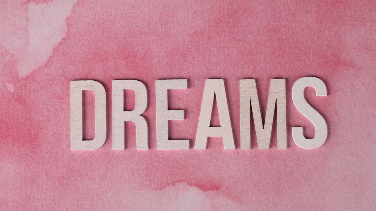 Inspirational 'DREAMS' text overlay on pink watercolor textured background.